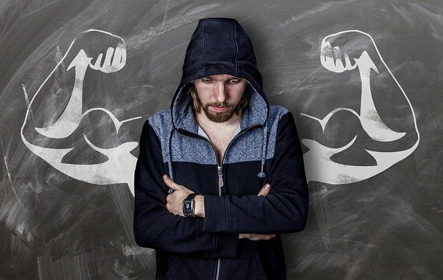 man in front of blackboard showing strong arms clenching muscles